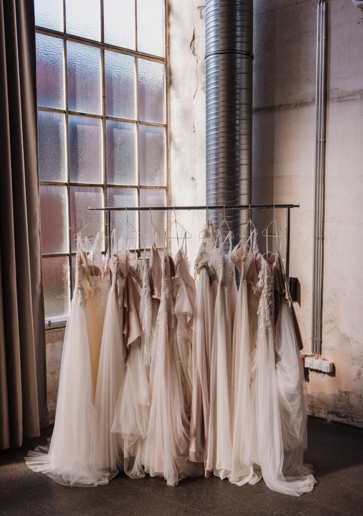 Brautkleider in verschiedenen Längen und Blushtönen auf einer KLeiderstange in einer industriellen Location mit großen Fenstern